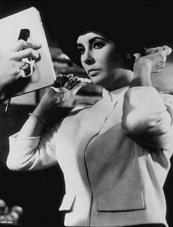 Elizabeth Taylor adjusts her hat during a break from filming