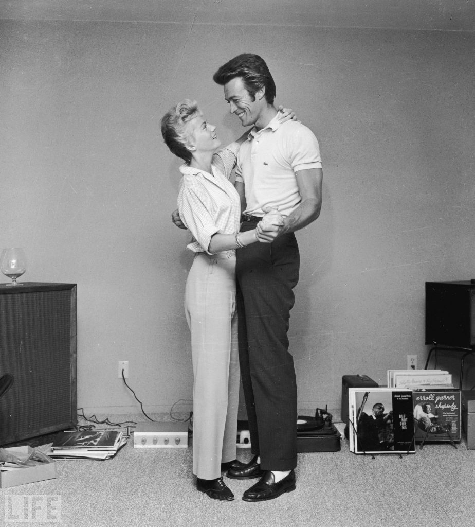 Clint Eastwood and his first wife, Maggie, dance next to a turntable and a rack full of records in a living room in 1965.