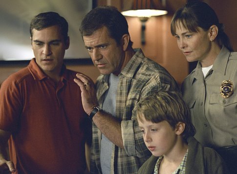 Graham (Mel Gibson, center), flanked by his brother, Merrill (Joaquin Phoenix, left), Officer Paski (Cherry Jones, right), and his son, Morgan (Rory Culkin, foreground), soon find that they are not alone - that crop signs are appearing all over the world