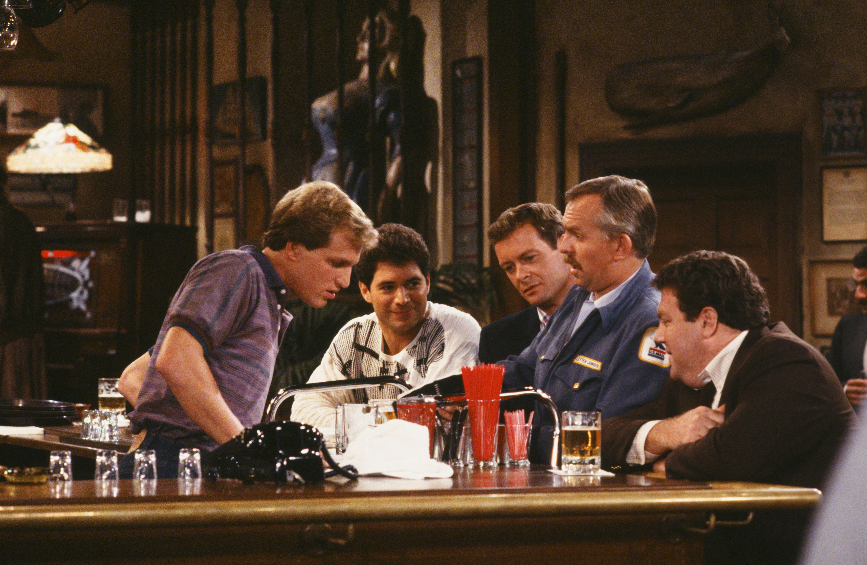 Still of Woody Harrelson, John Ratzenberger, George Wendt, Tim Cunningham, Steve Giannelli and Johnny Gilbert in Cheers (1982)