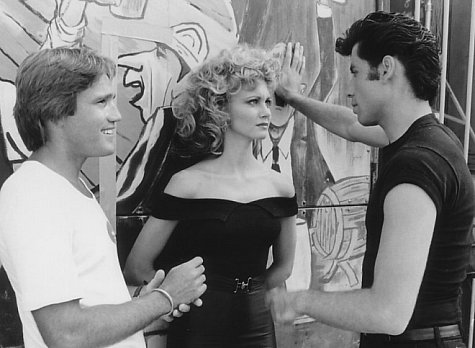 Director Randal Kleiser (left) with Olivia Newton-John (center) and John Travolta (right) on the graduation carnival set.