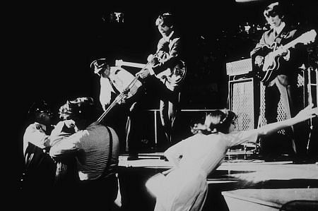 The Beatles (Paul McCartney & George Harrison) perfroming while security restrains fans from stage, c. 1964