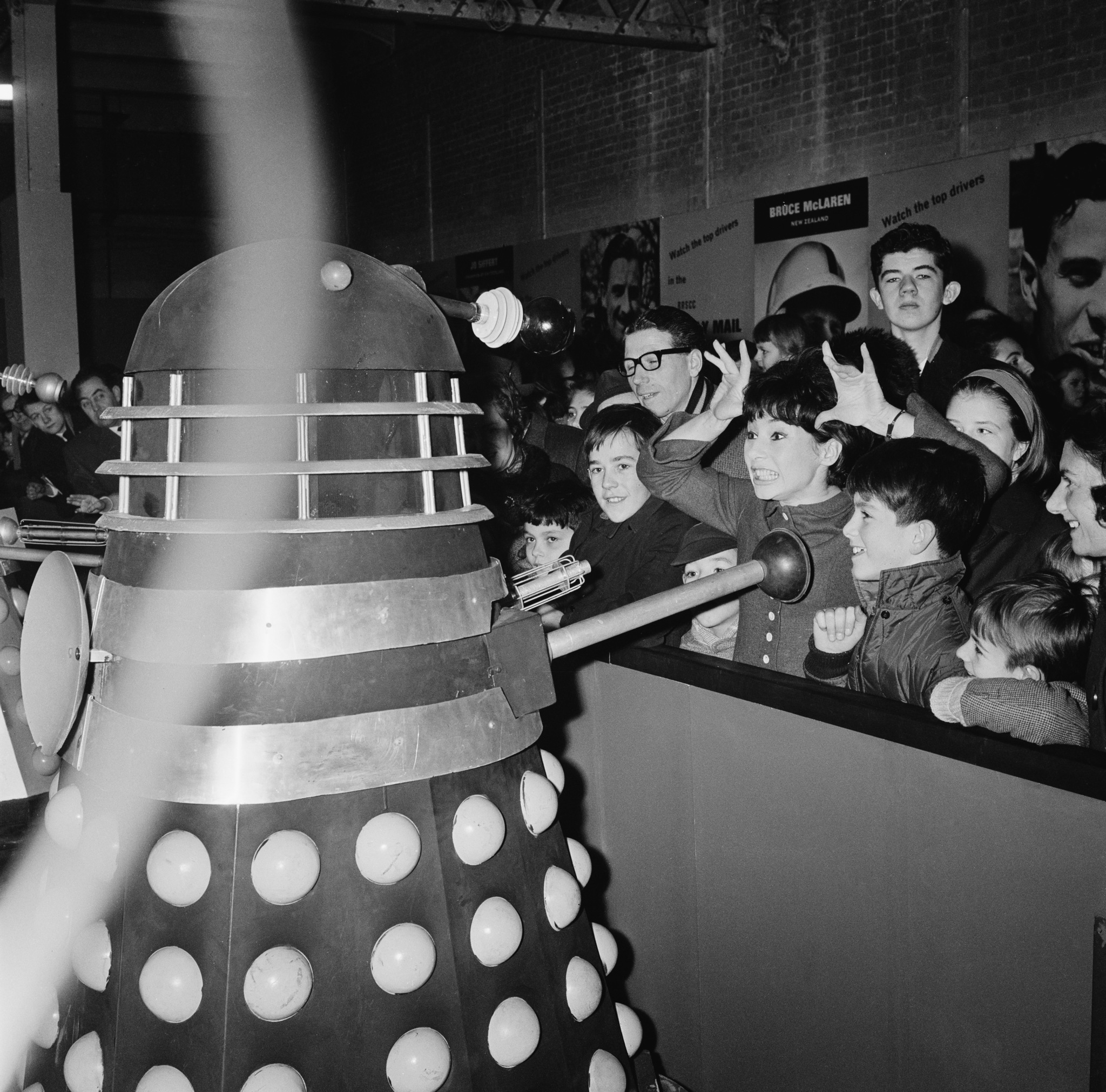 British actress Carole Ann Ford (centre, right) makes a horn sign at a Dalek from the BBC television science fiction series 'Doctor Who', at the Daily Mail Schoolboys' and Girls' Exhibition at Olympia, London, 28th December 1964. In the series, Ford plays Susan Foreman, the companion of the first Doctor, played by William Hartnell.