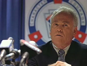President Sloan (Richard Fullerton) holds a press conference in 