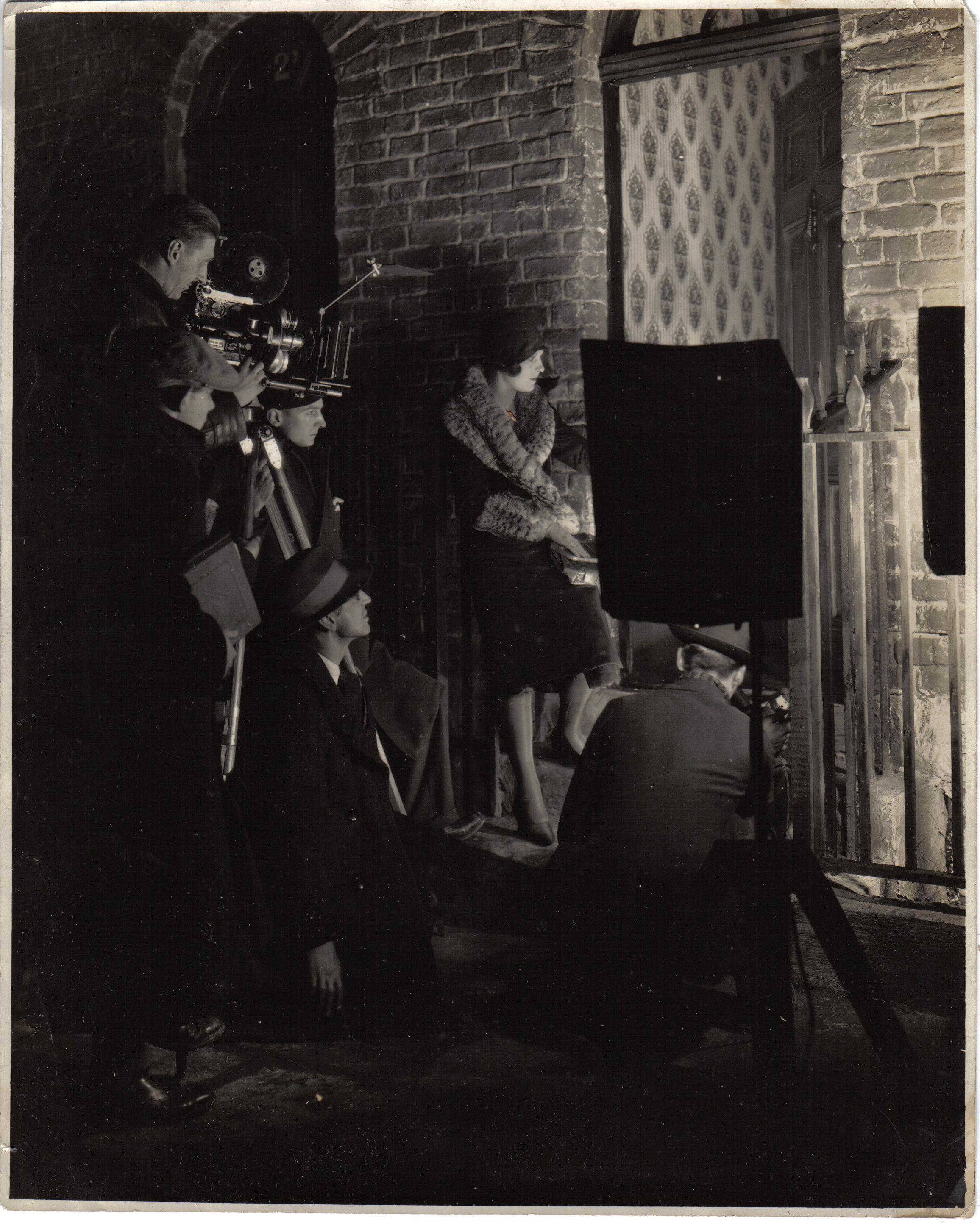 Edwin Greenwood wearing hat, kneeling, in profile, directing a film.
