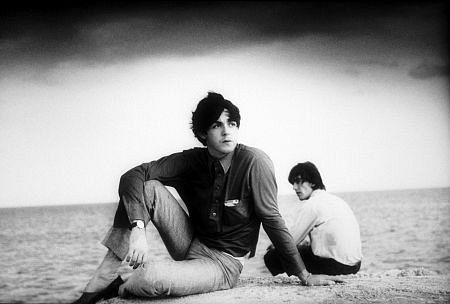 The Beatles (Paul McCartney, and George Harrison sitting on the sands) c. 1964