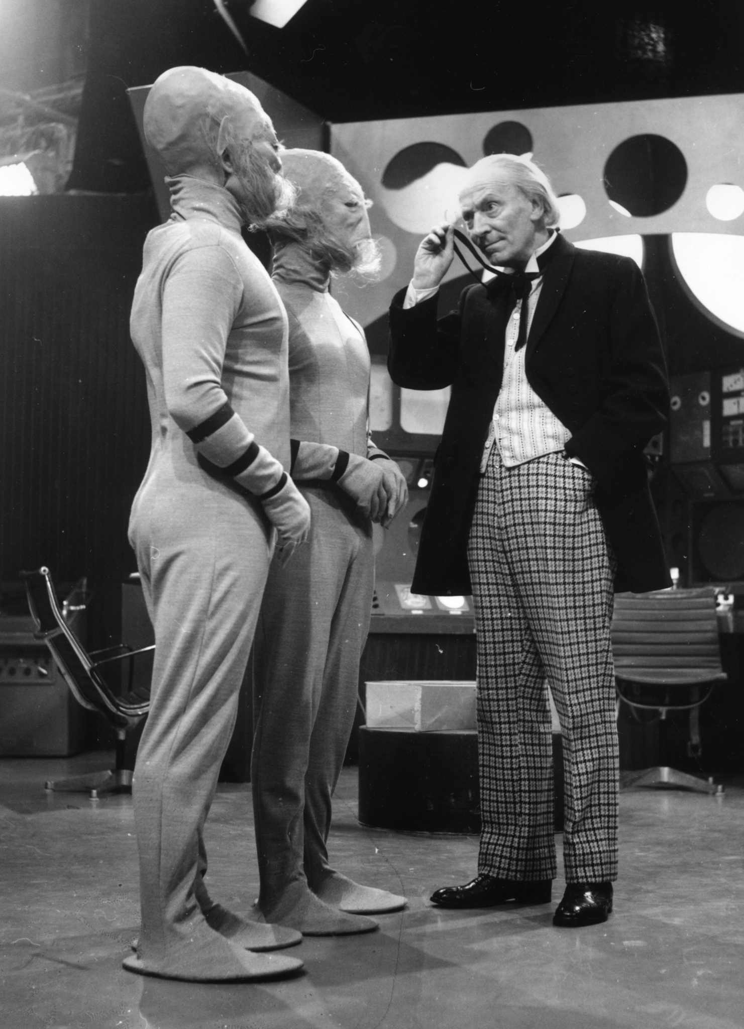 William Hartnell as Dr Who, peers through his monocle at two extra-terrestrials during filming of the popular science fiction series, 'Dr Who' at the BBC's Shepherds Bush Studios in London.