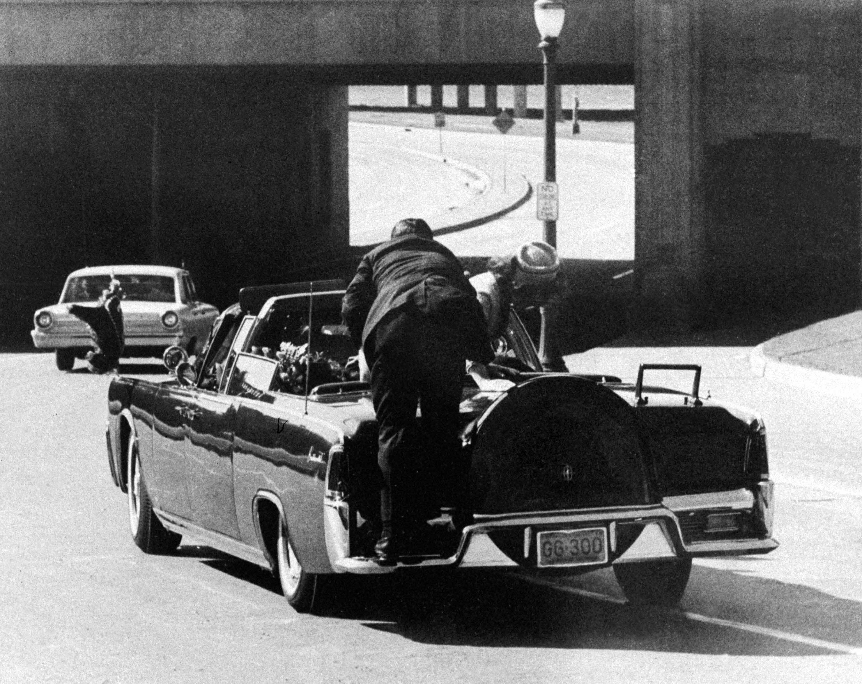 Secret Service Agent Clint Hill leaps aboard presidential limousine to shield JFK and Mrs. Kennedy as shots are fired in Dallas on 11.22/63