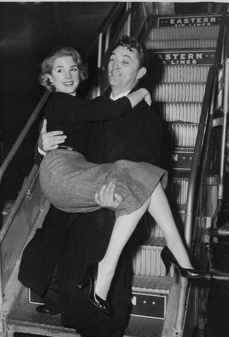 Karen Sharpe arrives in style, in the arms of Robert Mitchum at New York's LaGuardia Airport for the premiere of Man with the Gun