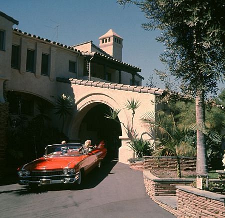 JAYNE MANSFIELD IN THE DRIVEWAY OF HER BEVERLY HILLS HOME IN HER 1959 CADILLAC WITH ONE OF HER KIDS