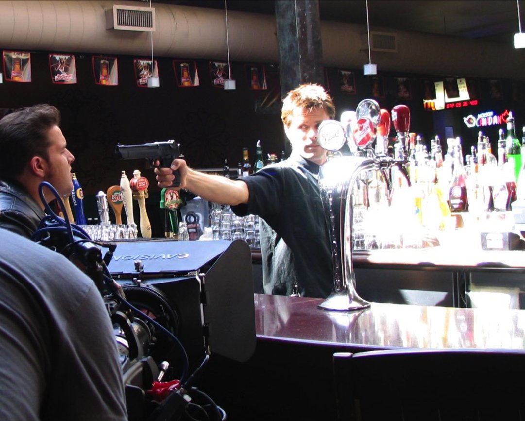 The Bartender (Douglas Kidd) points his gun at Don (Matthew Stefiuk) in a scene from Donkey (2010).
