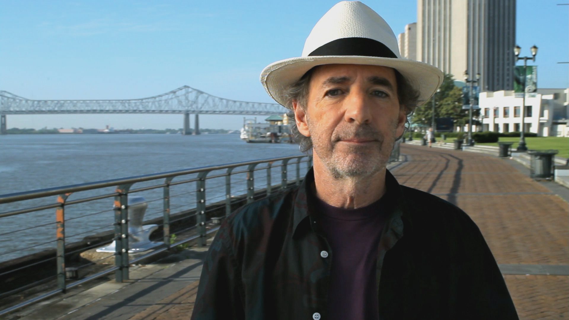 Harry Shearer, director of The Big Uneasy, in New Orleans on the bank of the Mississippi River with the Pontchartrain Expressway in the background.