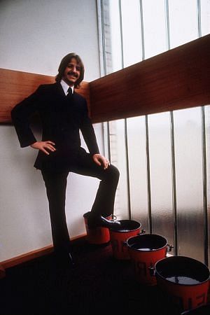 Ringo Starr in a suit resting his leg on a pail. c. 1969