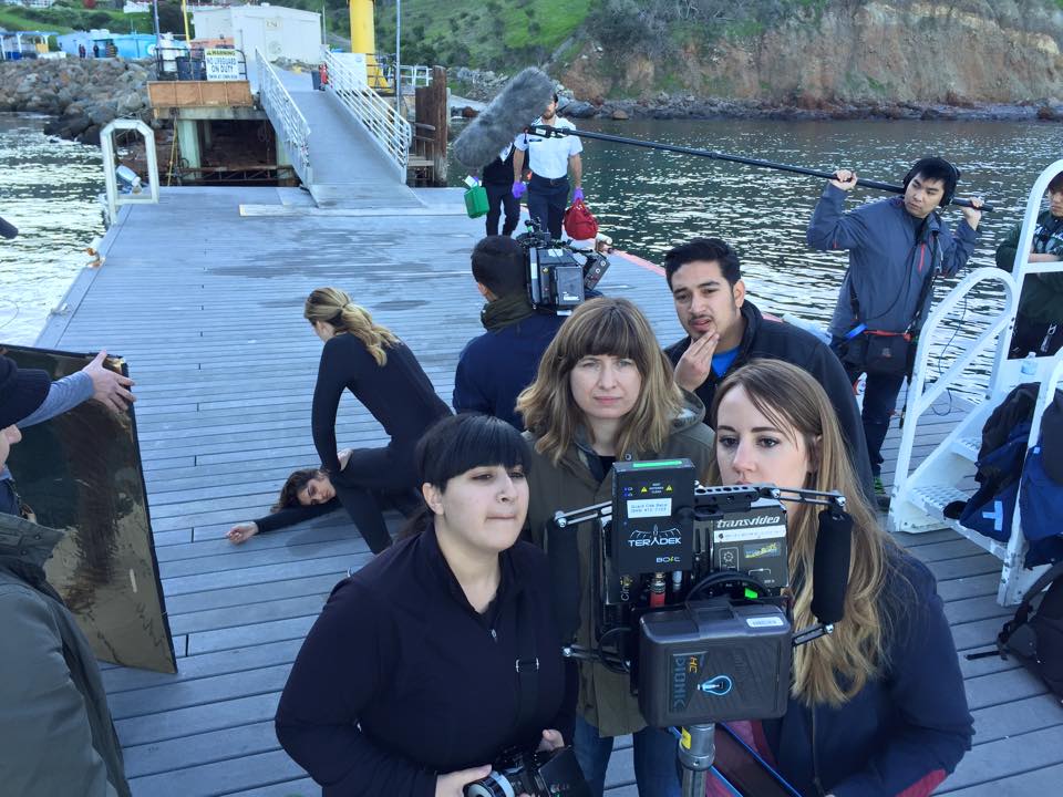 Director Amanda Tasse (center), Script Supervisor Amanda Griswald (right), 1st AC (Briana del Giorno), & AD Alan Manzo monitor a dock rescue scene in MIRA with actors Vanessa Patel (far left), Anne Dudek (far center), DP Xing-Mai-Deng (far center right).