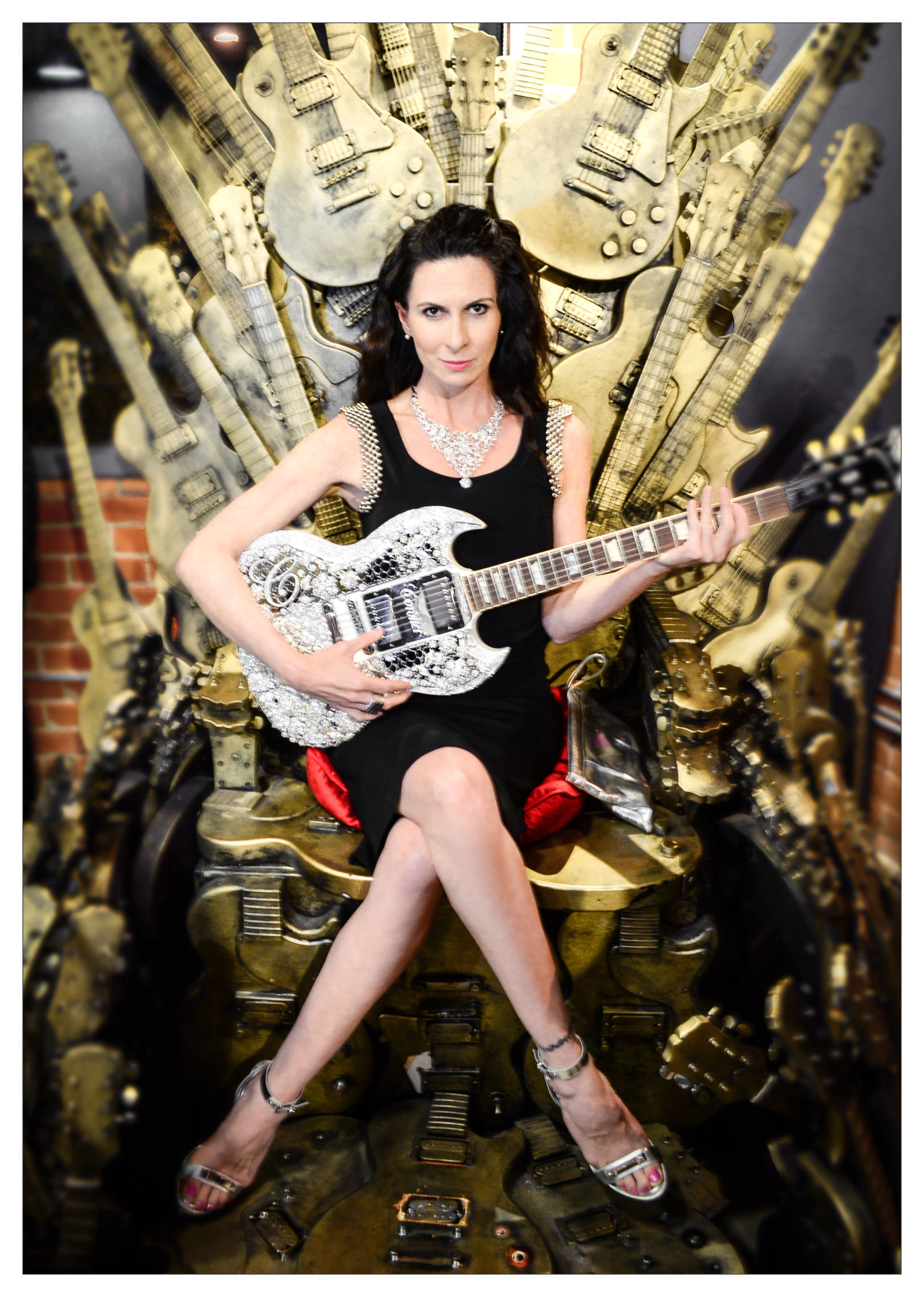 Stuntwoman Tammie Baird sitting on the Chair of Tones, holding a Gibson Guitar valued at $2 million, it is encased in gorgeous diamonds. It also holds a Guinness book world record for its value. The necklace is by Coronet Diamonds.