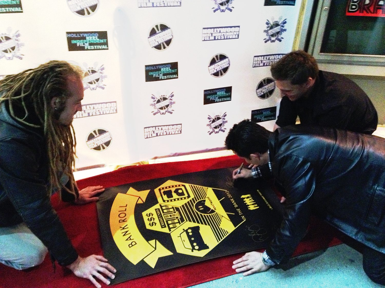 (L-R): Azmyth Kaminski, Josh Roman and Doug Maguire sign the film festival poster on the red carpet for their movie Bank Roll at the 2012 Hollywood Reel Independent Film Festival.