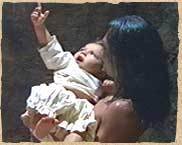 Baby Jesus (Juan-Salvador Carrasco) points towards heaven, as he is embraced by Topiltzin (Damián Delgado) in 
