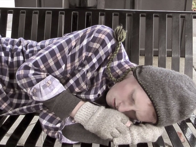 A hobo (Brandon Burns) sleeps on a park bench near the train station.