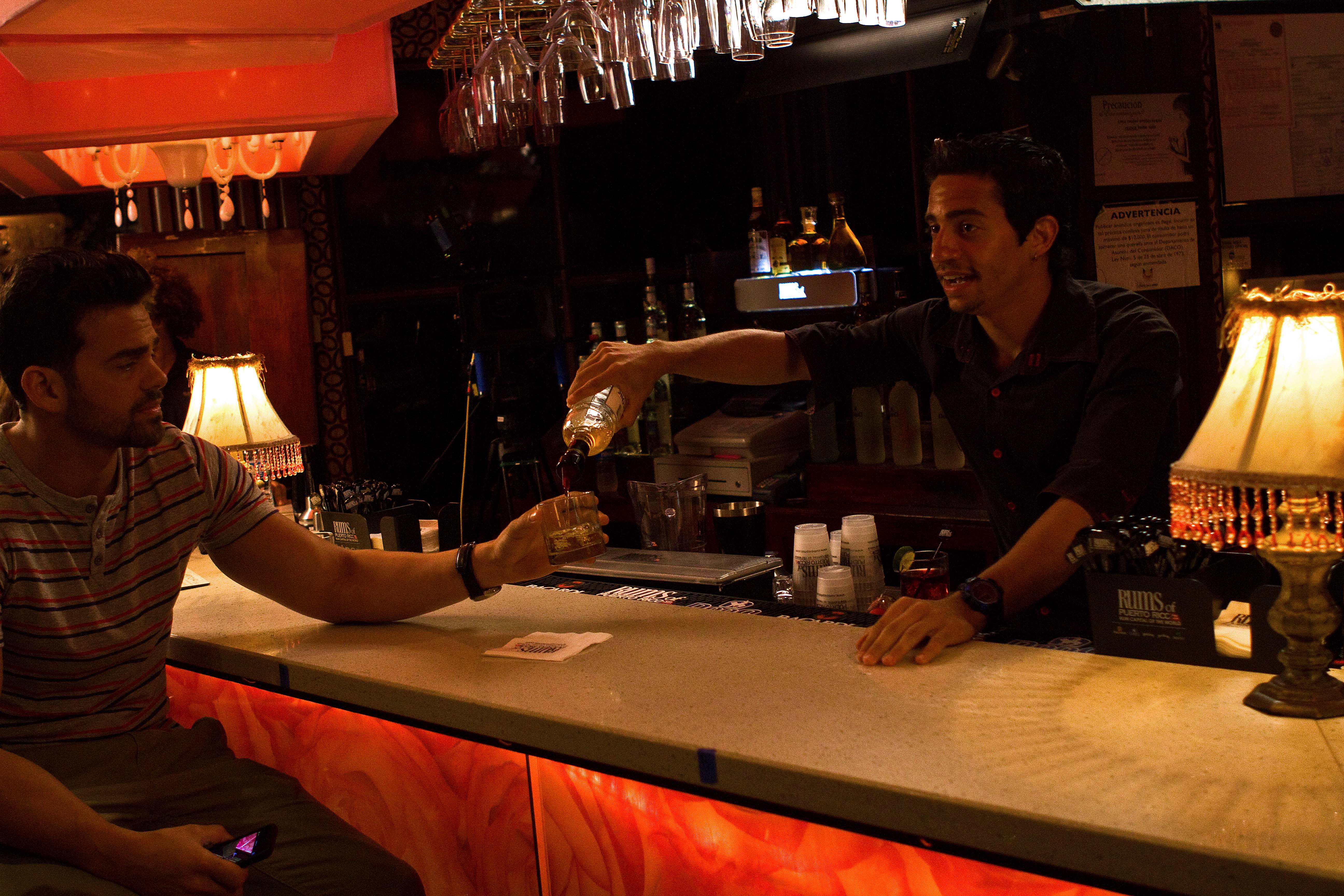 Monchi, the bartender, serves a drink to Alejandro Cuevas, in the Telemundo TV series, Incógnita.