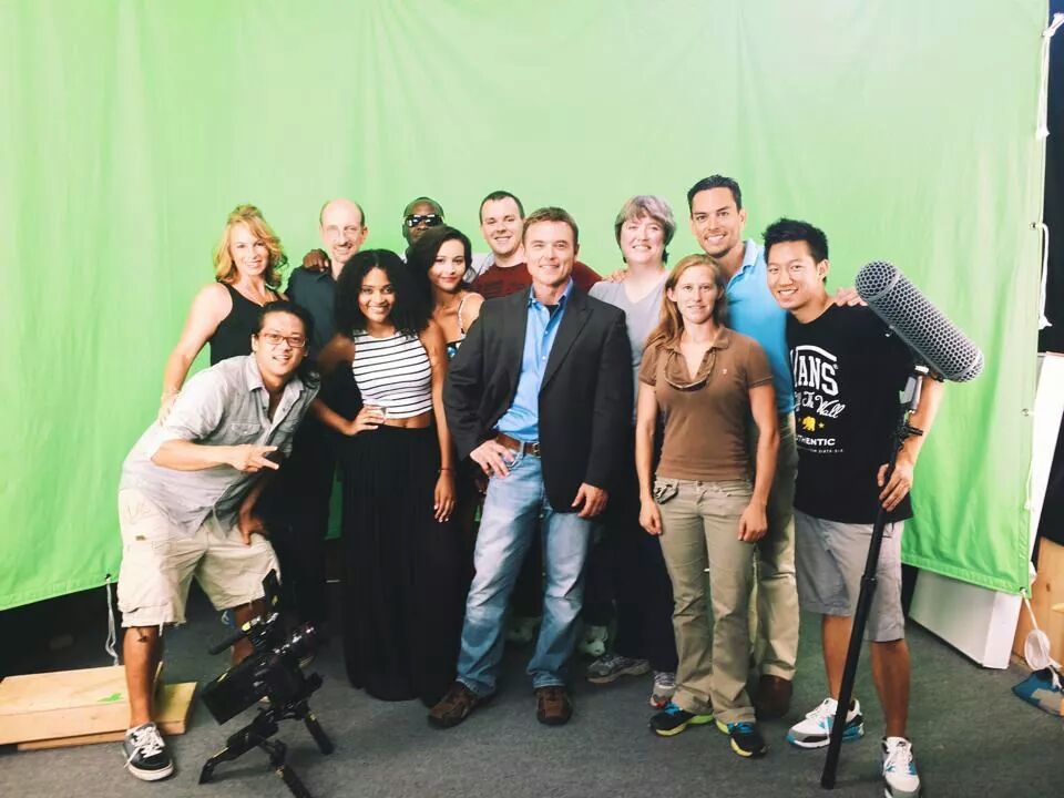 Behind the scenes on a green screen set with cast and crew.