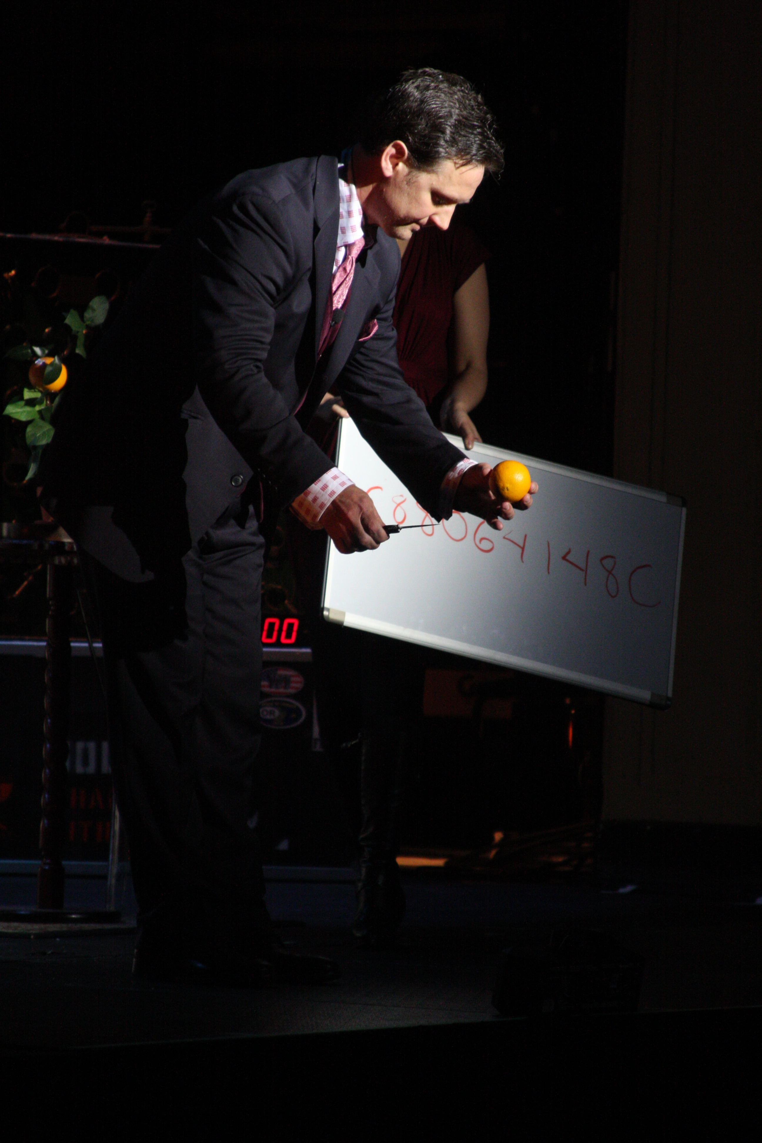 Magicially transforming a borrowed dollar bill from a spectator's pocket inside of an orange. On stage performing at the 2011 Salute To Magic in New York City.