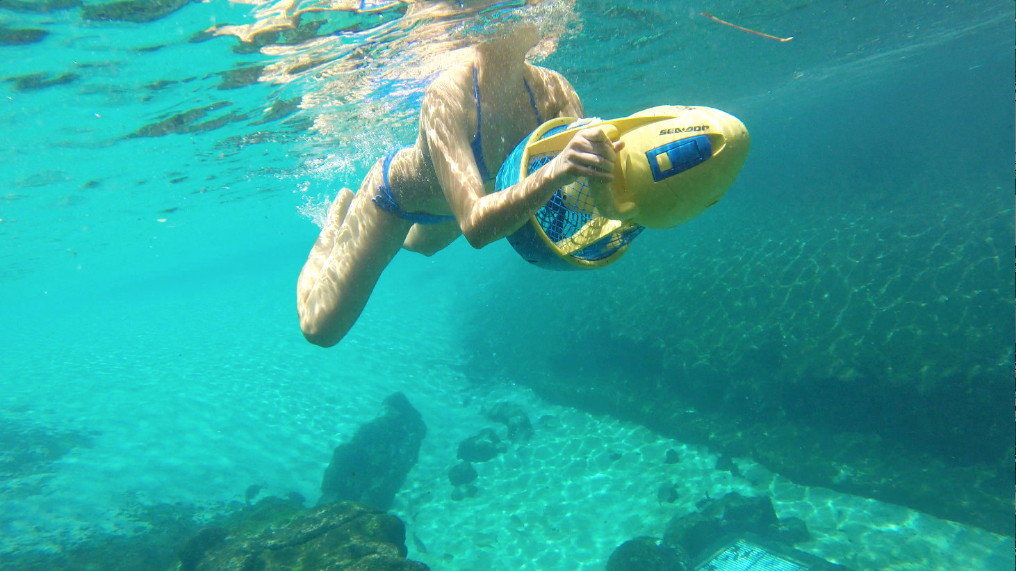 A Still of Emily Whitechurch riding a Sea scooter in a tropical reef pool.