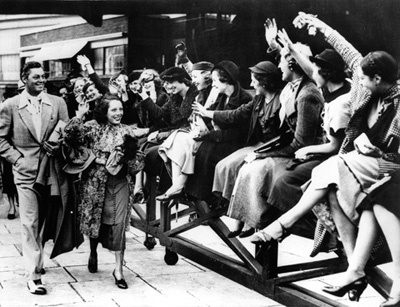 Johnny Weissmuller and Lupe Velez arriving at Paddington Station in London as admirers cheer 10-12-1934