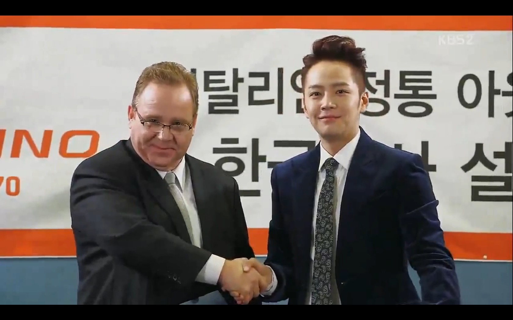 Still of Dean Dawson as CEO Richard Rose shaking hands with Dok-go Mate (Jang,Geun-seok) as the most beautiful man in the world on KBS television.