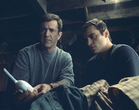 A baby monitor provides a message from above for Graham (Mel Gibson, left) and his brother, Merrill (Joaquin Phoenix, right).