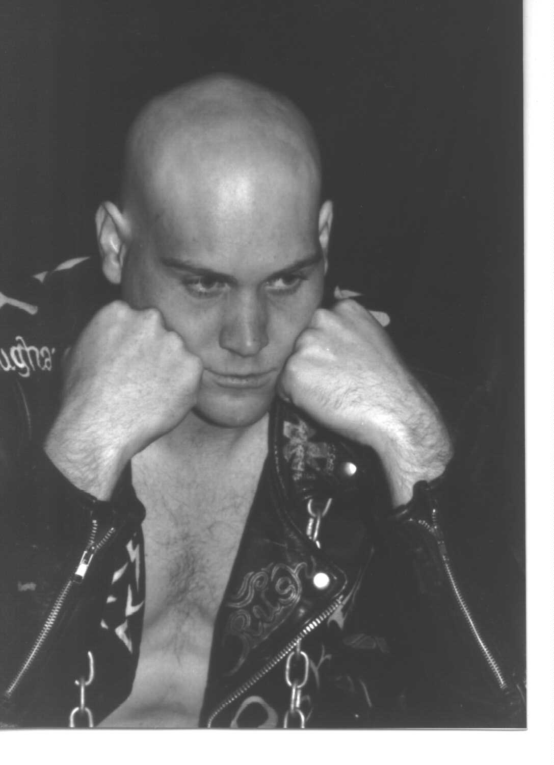 Hawke with shaved head in biker jacket.