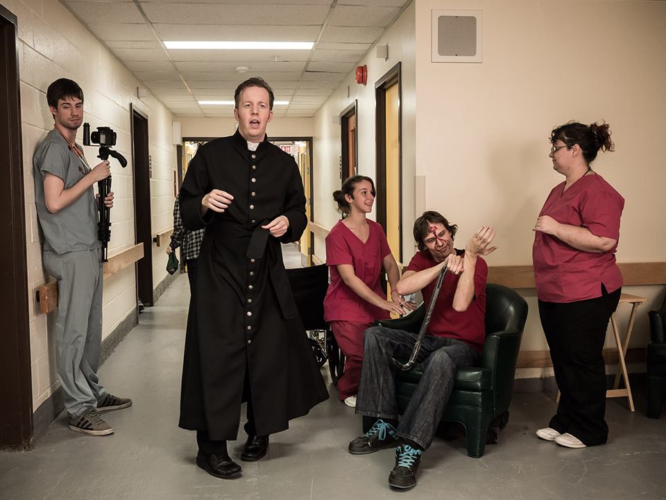 Ryan (center, in costume as Father Bane) directs his crew and background actors on the set of Holy Hell.