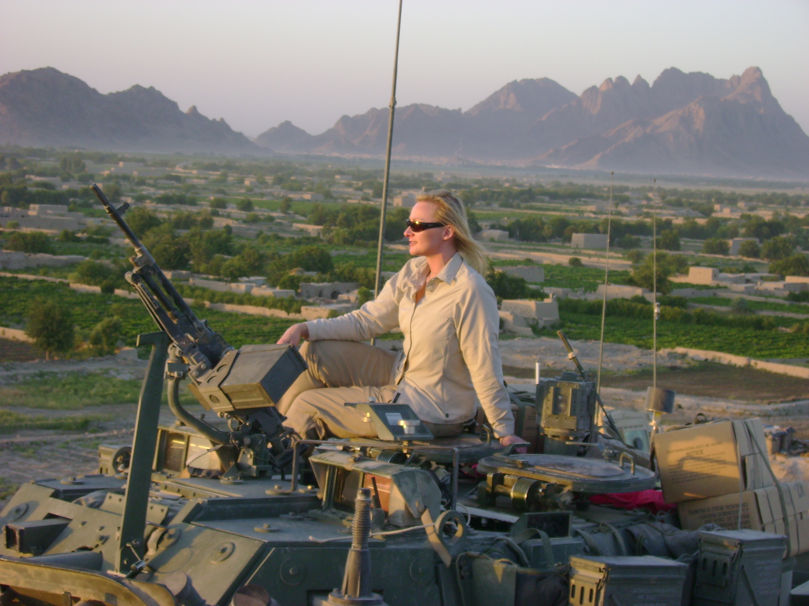 War Reporter Alex Quade watching battle in valley below from armored vehicle, while shooting 