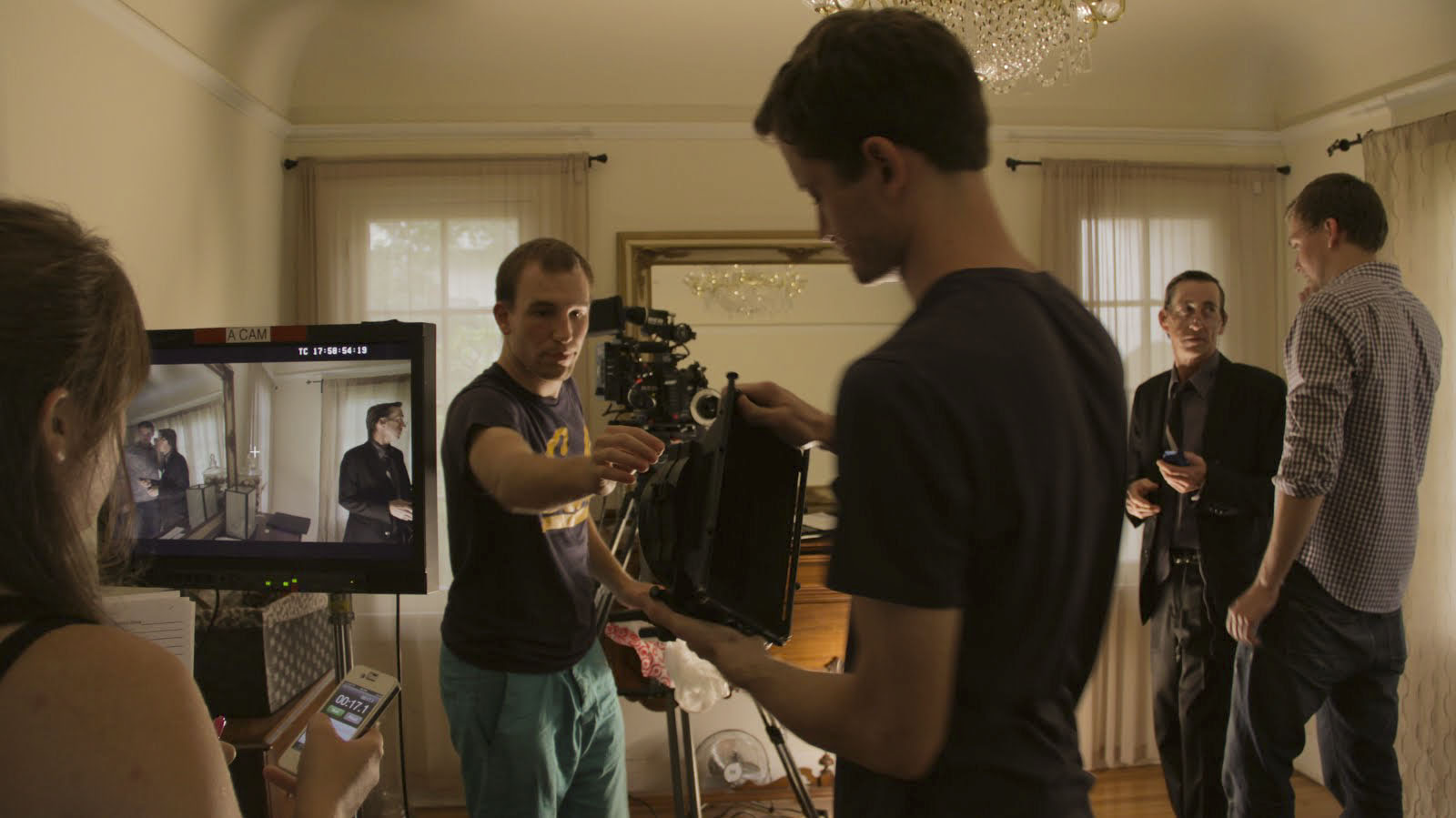 On the left, Tobias Deml and assistant cameraman Nathan Francis pass the matte box to assemble the camera, while on the right, actor Jimmy McFinn and David Leidy discuss the scene.