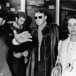 Richard Burton and Elizabeth Taylor being escorted by a policeman at Romes Leonardo da Vinci airpport on departure for Lecce Southern Italy 11181972