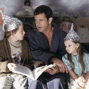 Graham Mel Gibson center tries to calm his children Morgan Rory Culkin left and Bo Abigail Breslin right who think that tin foil hats can stop aliens from reading their minds
