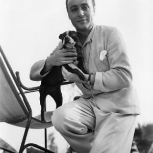 Charles Boyer holding his pet terrier Nip in the garden of his home
