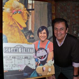 Emilio Delgado poses next to his character Luis' photo, that marked Sesame Street's 1000th episode. Photo dates: Jan 26, 1977 and January 14, 2008.