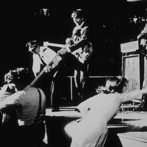 The Beatles (Paul McCartney & George Harrison) perfroming while security restrains fans from stage, c. 1964