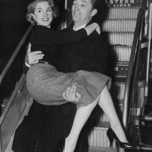 Karen Sharpe arrives in style, in the arms of Robert Mitchum at New York's LaGuardia Airport for the premiere of Man with the Gun