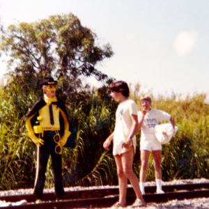 Jon Teboe center directs Jennifer Ashlock The Girl and Steve Frazier The Yellow Ranger in a scene for The Yellow Ranger on the train tracks in Miami Florida Dan Frazier far right is assisting with the props 1983 Miami Florida