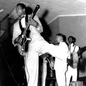 Chuck Berry in full flight with Johnny Greenan on tenor sax and Lou Nanlohy on guitar supporting in the back ground Melbourne Festival Hall in 1958