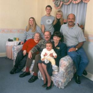 The Cast of Looking After the Penneys. Back l - r Sarah Roberts, Jonathan Howard, Samatha Hilton, James Crompton. Front l - r Susan Briers, Dave Dutton and Hazel Cadman as Sally Penney with baby Lara (Alayah Worden).