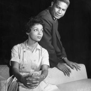 Married American actors Ruby Dee left and Ossie Davis sit on a sofa in front of a black background in a still from the television play Seven Times Monday