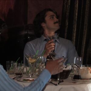 Billy (Sean Carlin), wearing a fake moustache, orders another round of amaretto and pineapple while Paul (Josiah Lipscomb) shows his fake room key to charge the drinks to his hotel room.