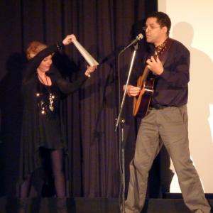 Esther Kreis holds poetic lyric sheet up to Jeffrey Day (Voice Over Actor of DISPLACEMENT)as Jeffrey performs his song PRAYER TO THE ISLAND he composed for the European Film Premiere.