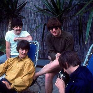 The Beatles Paul McCartney George Harrison John Lennon Ringo Starr watch as Ringo fools around with his camera 1964