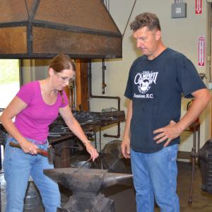 Ann Lukens interviewing blacksmith Paul Garrett and trying a hand at the hammer.