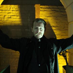 actor LEW TEMPLE playing Father Elias Solomon preaching lessons and rituals to the character Jackson Kincade played by BRYAN DAVID in the movie House of Forbidden Secrets