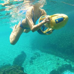 A Still of Emily Whitechurch riding a Sea scooter in a tropical reef pool.