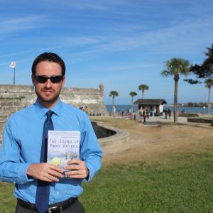Sean Bloomfield with his novel, The Sound of Many Waters, at one of the settings in the book: St. Augustine, Florida.
